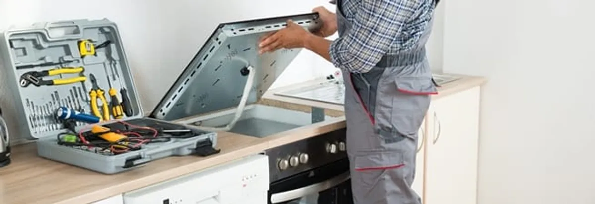 Cooktop repair technician lifting a built-in stovetop for service in Stamford, CT